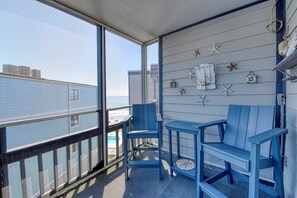 A balcony with a view of the ocean, blue chairs, a small table, and decorative starfish on the wall.
