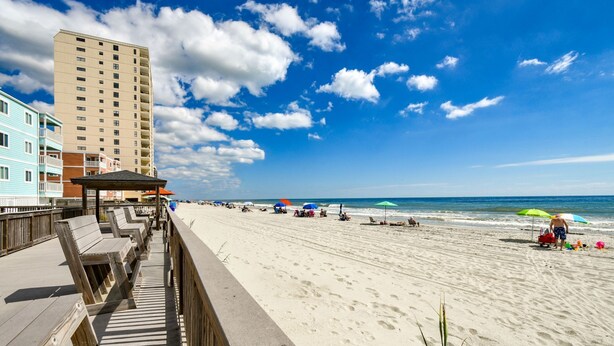 A beach with a wooden boardwalk, a tall building, and beach umbrellas. - Sea Oaks 308 - Two Bedroom, Two Bath Corner Oceanfront Condo (Garden City Beach)