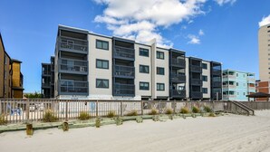 A multi-story residential building with balconies, a wooden fence, and a sandy beach in the foreground. - Sea Oaks 308 - Two Bedroom, Two Bath Corner Oceanfront Condo (Garden City Beach)
