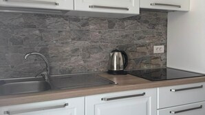A kitchen with white cabinets, a stone backsplash, a stainless steel sink, and a kettle. - Sormano 2 - THE V Collection Apartment by OGS (Sormano)