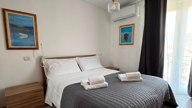A neatly made bed with a dark quilt, a bedside table, a wall-mounted air conditioner, and two framed artworks. - Sormano 2 - THE V Collection Apartment by OGS (Sormano)