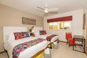 A hotel room with two beds, a desk, a chair, a ceiling fan, and a window with a red valance.