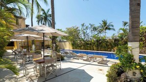 A poolside area with lounge chairs and umbrellas, surrounded by palm trees and a clear blue sky. - Sleeps 6, Views & Beach 1 Block (Nuevo Vallarta)