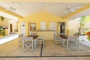 A covered outdoor seating area with tables and chairs, ceiling fans, and potted plants.