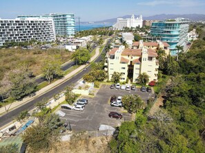 A multi-story hotel with a parking lot, surrounded by greenery and a coastal view.