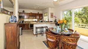 A spacious kitchen with dark wooden cabinets, a central island with stools, and a dining area with a round table and wicker chairs. - Sleeps 6, Views & Beach 1 Block (Nuevo Vallarta)