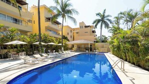 A swimming pool with lounge chairs and umbrellas, surrounded by palm trees and a multi-story building. - Sleeps 6, Views & Beach 1 Block (Nuevo Vallarta)