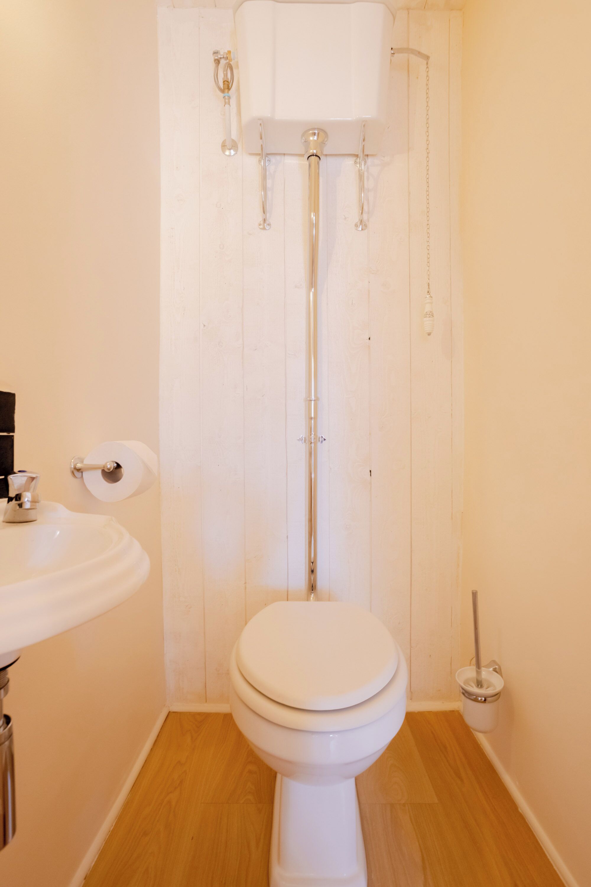 A small, clean bathroom with a white toilet, a sink, and a toilet paper holder.