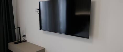 Et fladskærms-tv monteret på væggen, med en fjernbetjening på et lille bord nedenunder.