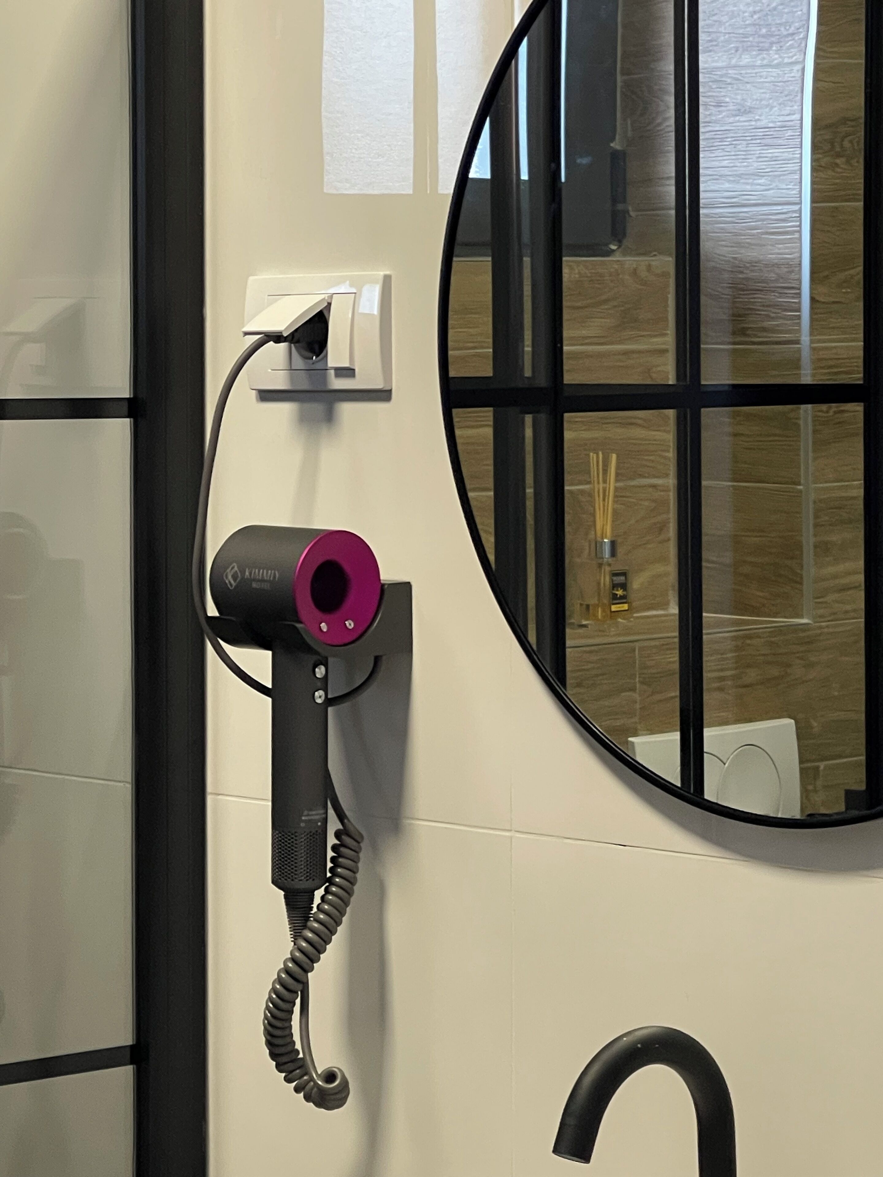 Une salle de bain avec un grand miroir, un robinet noir et un sèche-cheveux fixé au mur.