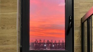 A framed picture of a sunset with trees and lights on a wooden wall. - KIMMIY HOTEL (Belgrade)