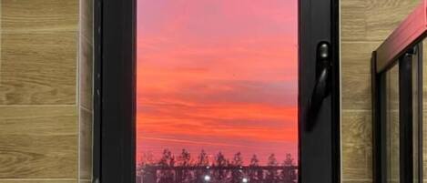 A framed picture of a sunset with trees and lights on a wooden wall.