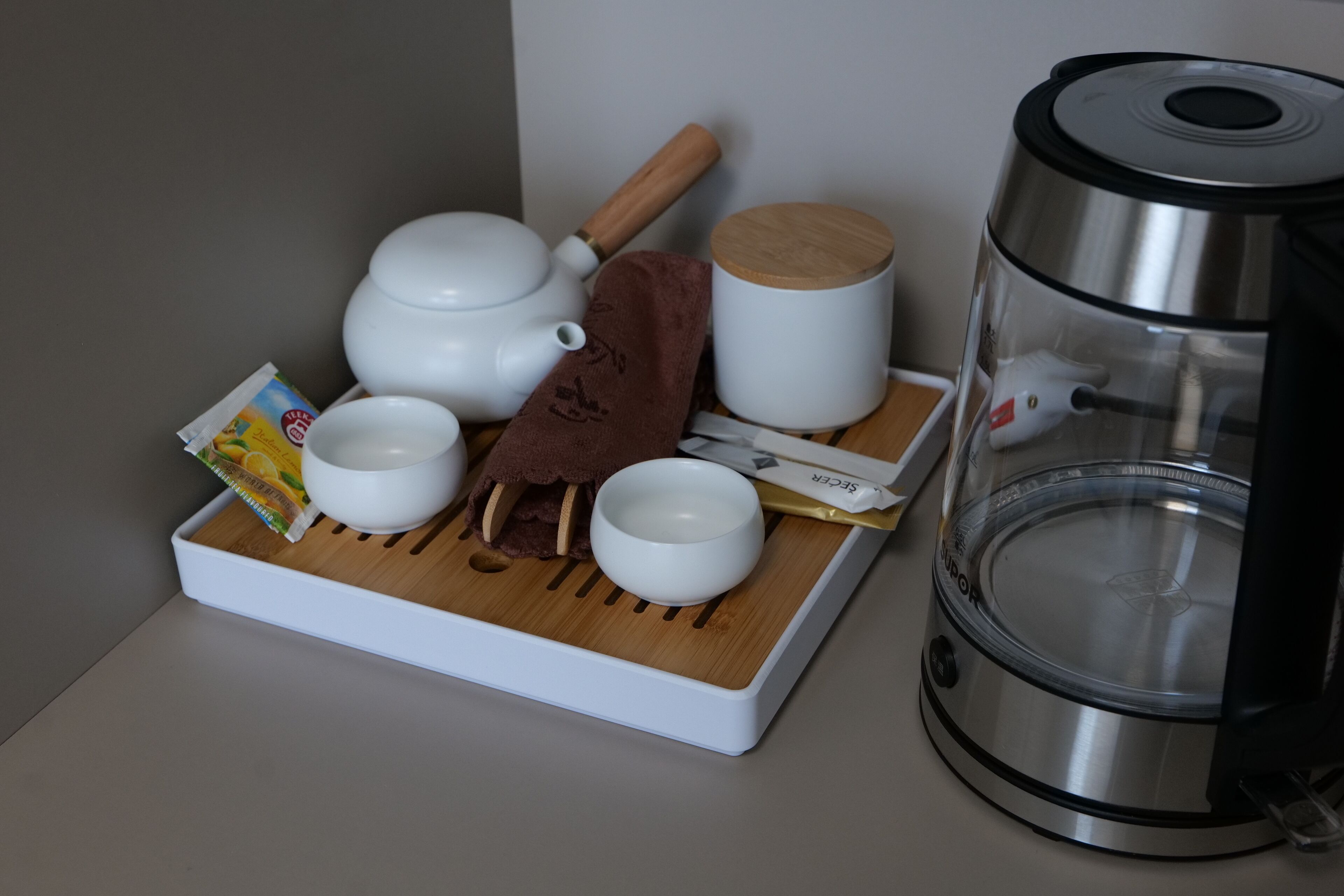 Una vajilla de cocina con tetera, tazas, una bandeja de madera, hervidor y un paquete de té.