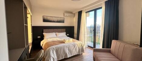 Una habitación de hotel moderna con una cama grande, un sofá, una puerta corrediza a un balcón y una lámpara en el techo.