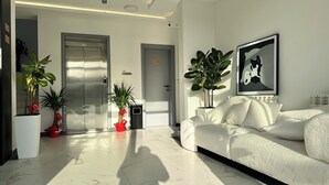 A modern living room with a white sofa, two potted plants, and a framed artwork on the wall. - KIMMIY HOTEL (Belgrade)