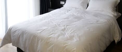 A modern hotel room with a large bed, a mounted air conditioner, a painting on the wall, and a view of the outdoors.