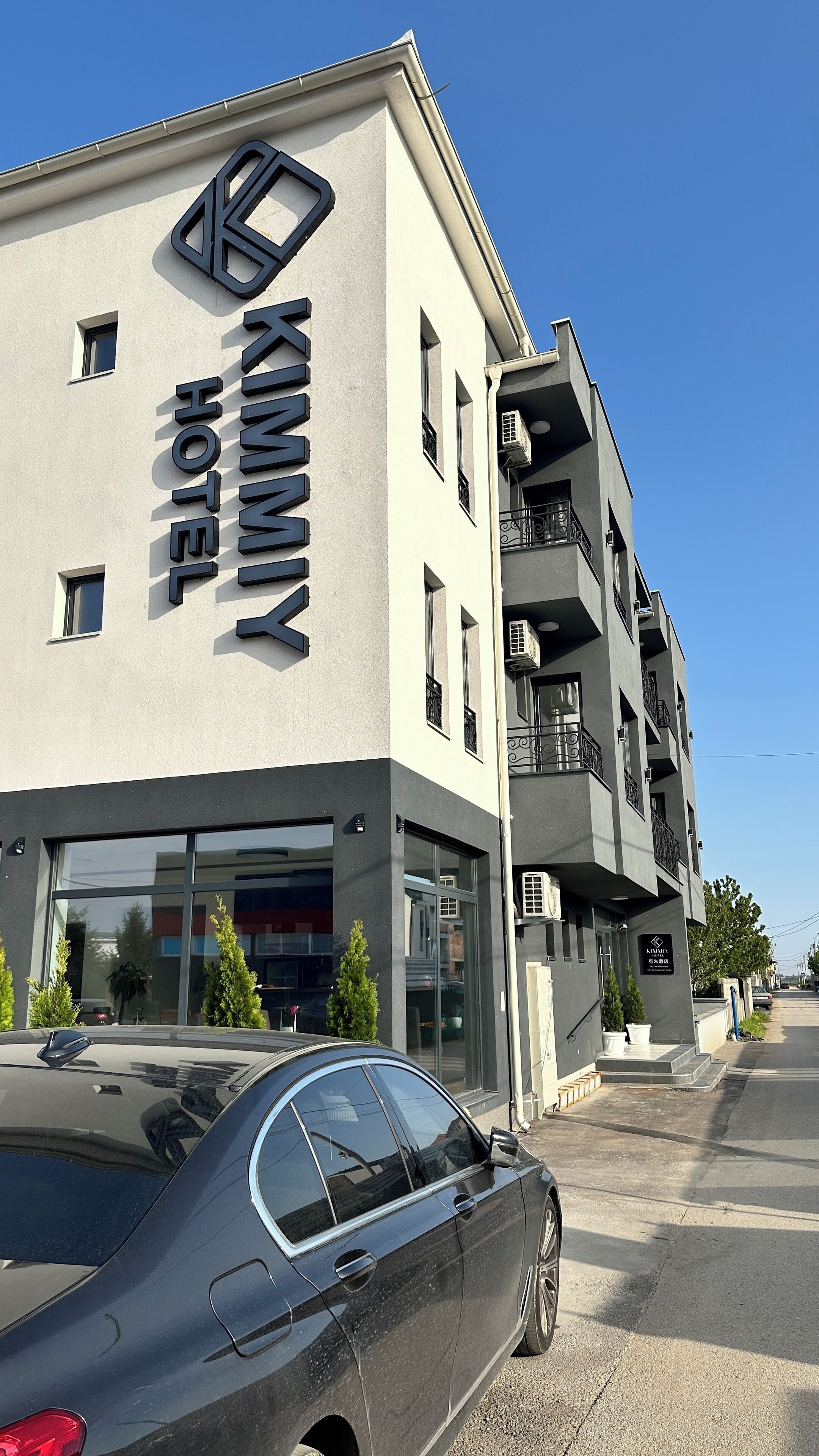 A hotel named "Kimmy Hotel" with a modern facade, large windows, and a car parked in front.