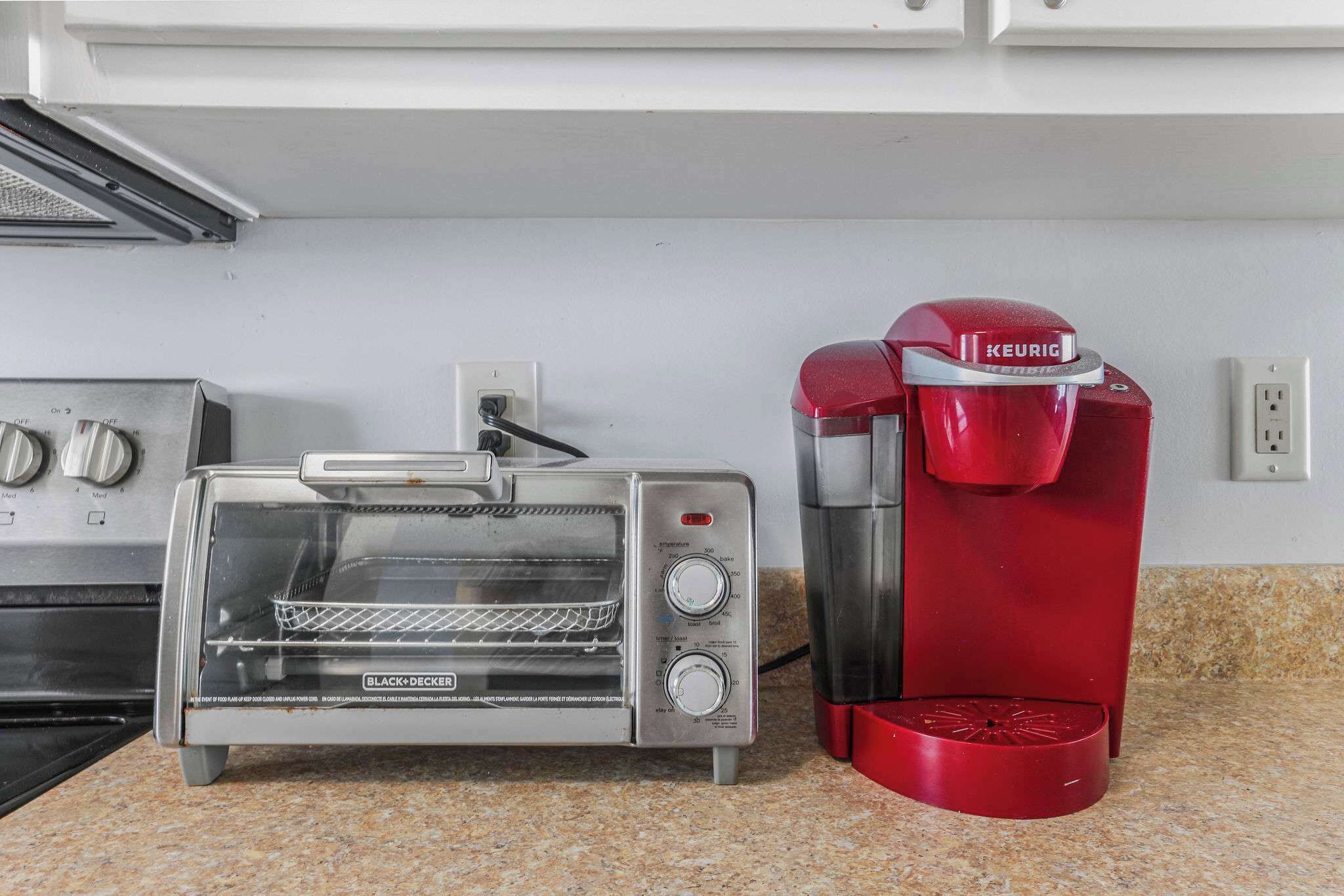 Una cocina con horno tostador y una cafetera Keurig roja sobre una encimera de granito.