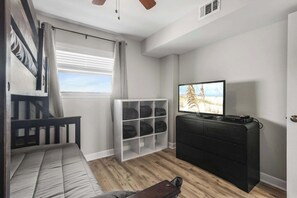 A room with a bed, a television, a storage unit, and a window with blinds.