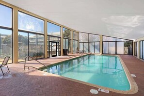 An indoor swimming pool with clear glass walls, a tiled floor, and a pool ladder.