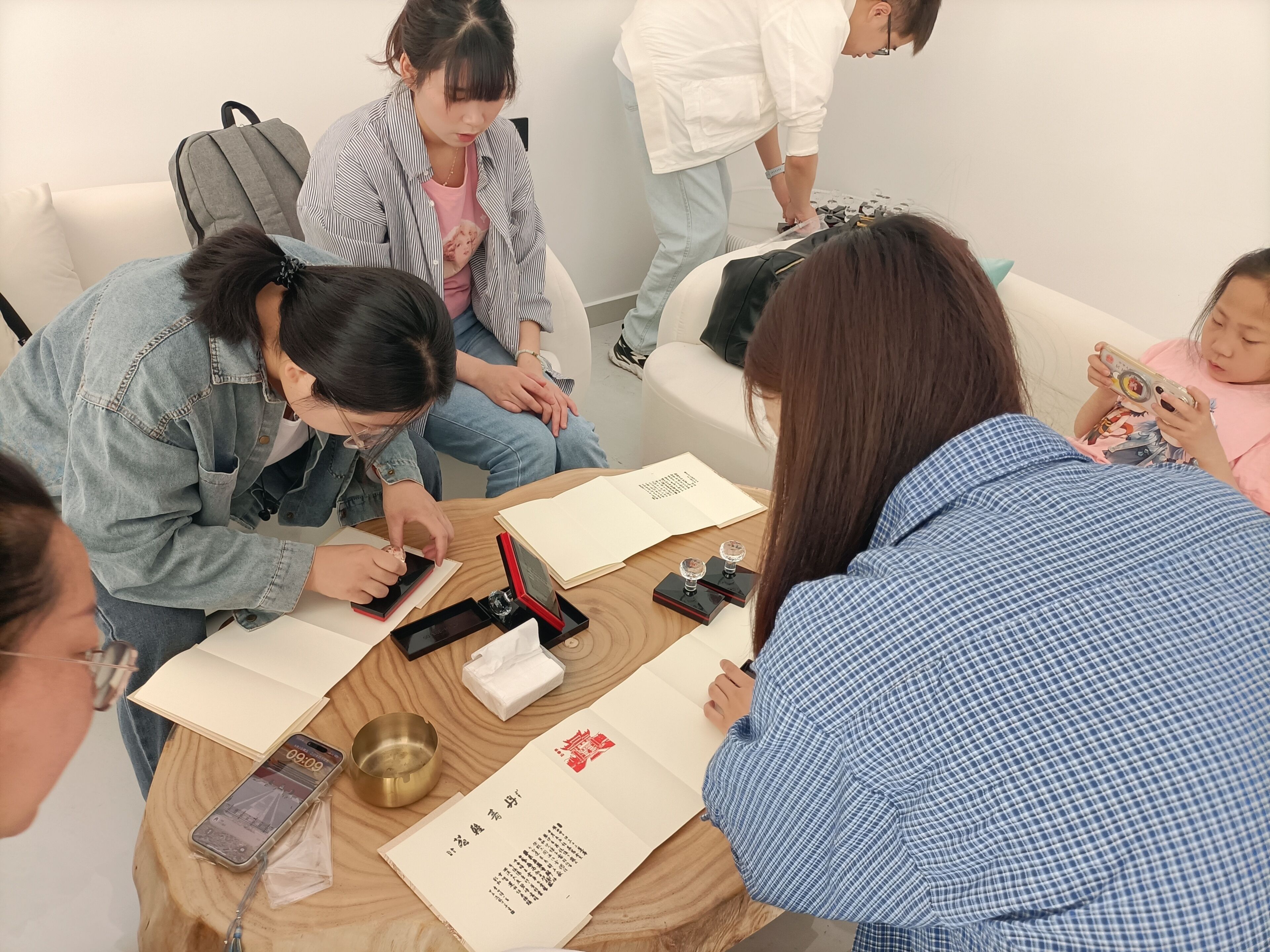 A group of people seated around a table with notebooks, pens, and a smartphone.