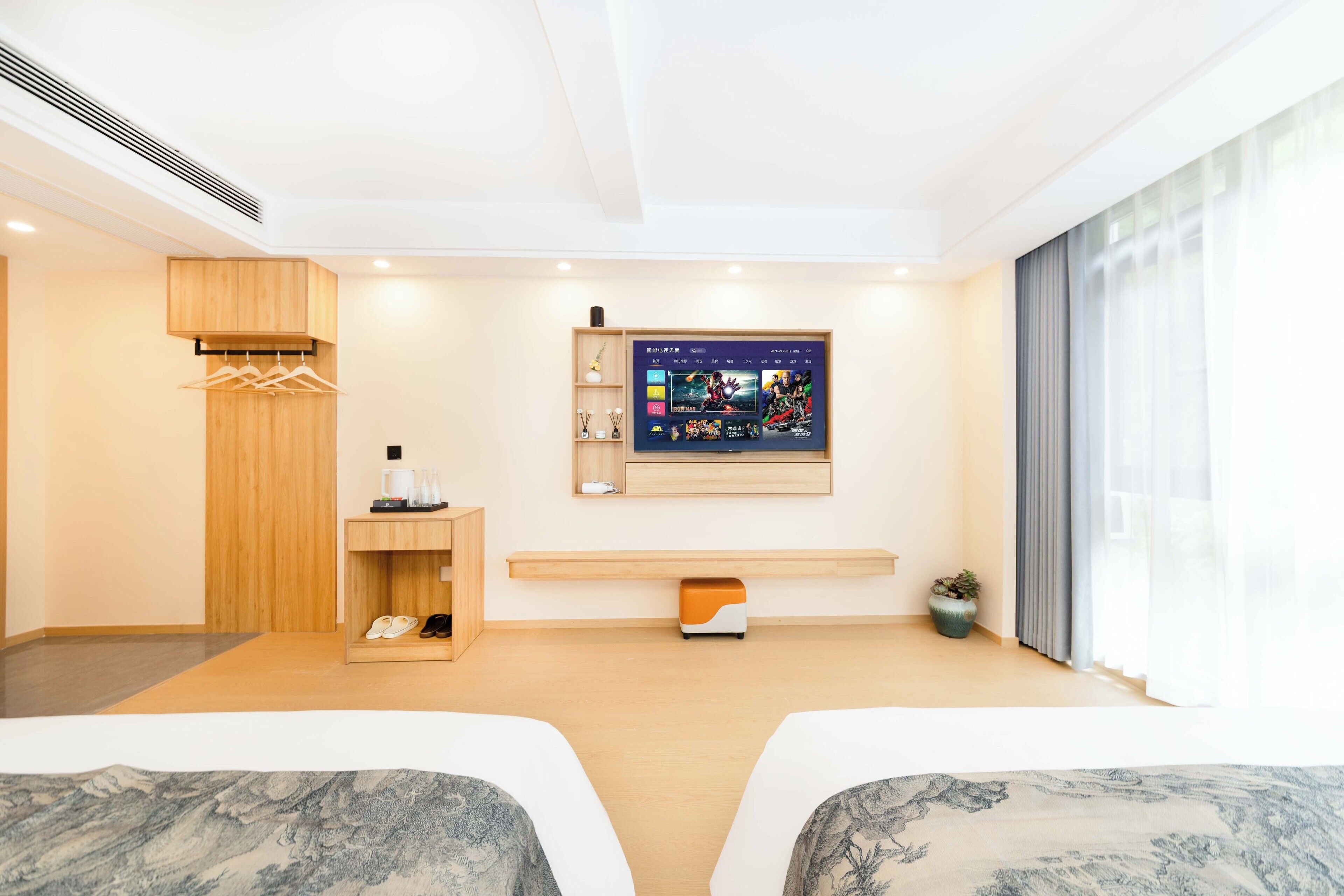 A modern hotel room with two beds, a mounted TV, a wooden cabinet, and a small shelf with personal items.