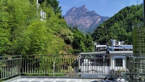 A terrace with a view of mountains, surrounded by greenery and a metal railing. - Mount Huangshan Danqing Yayuan B&B Hotel (Huangshan)