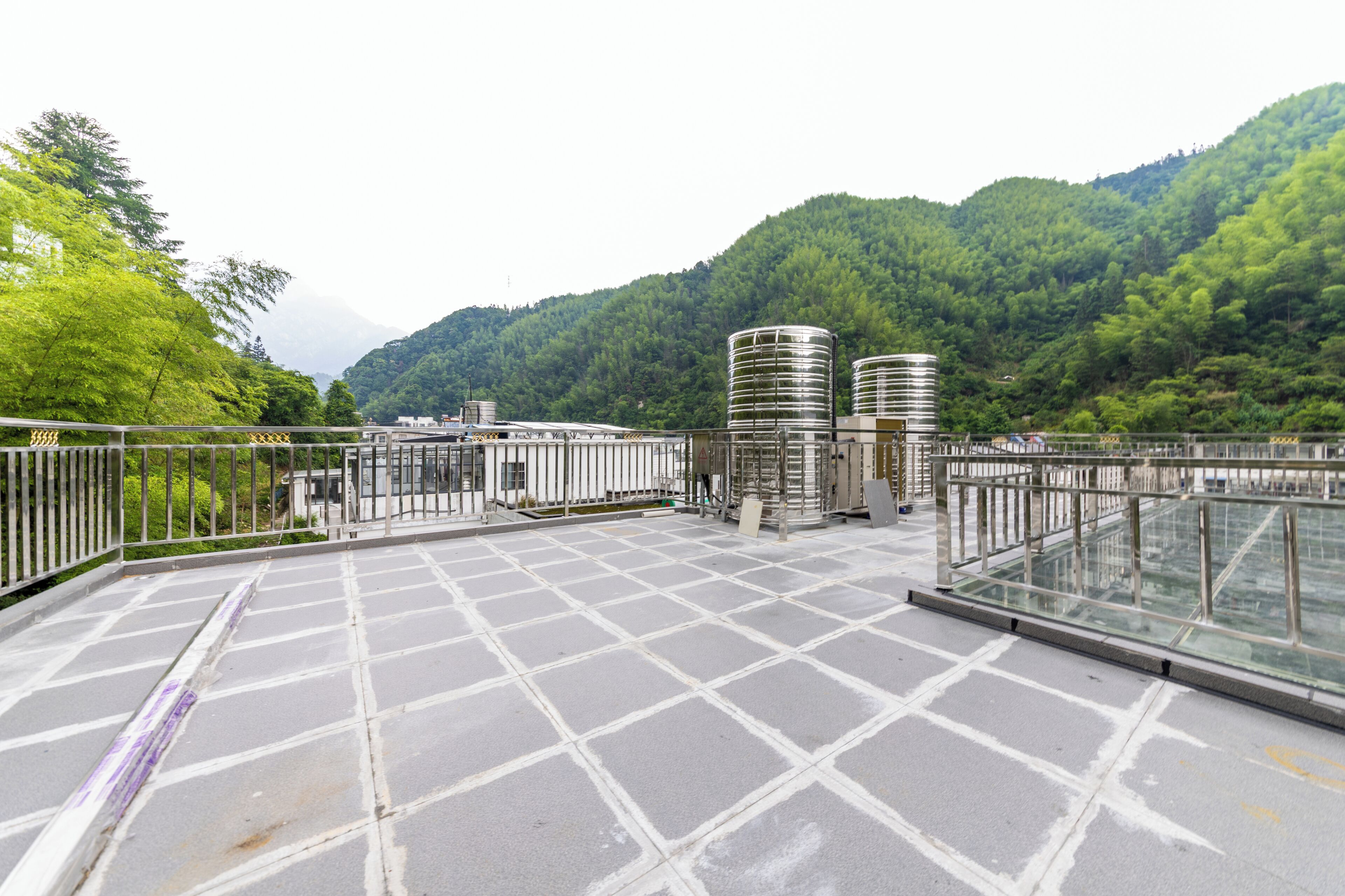 Een terras op het dak met een vloer in rasterpatroon, metalen hekwerk en cilindervormige constructies.