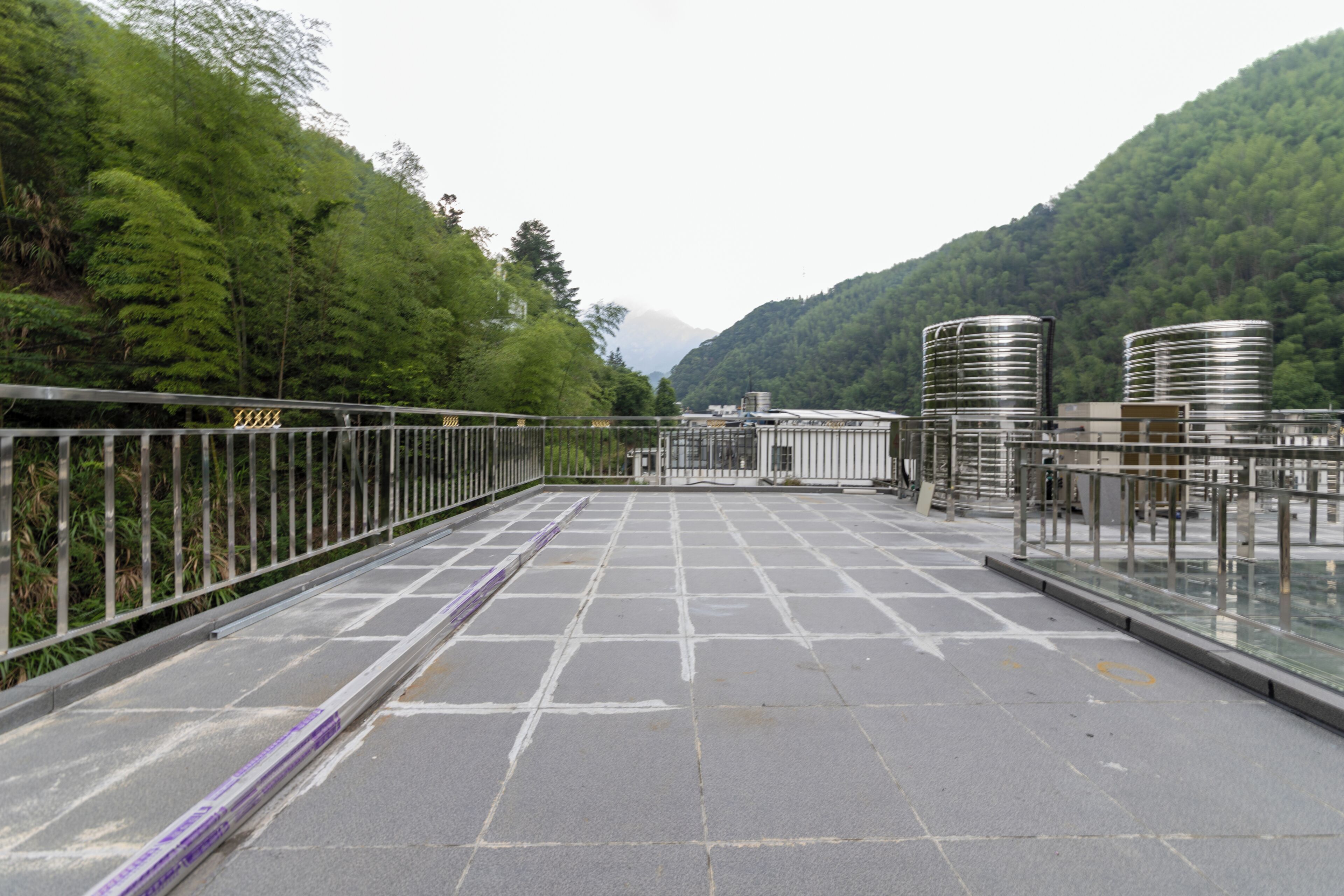 Ein gepflasterter Weg mit Metallgeländern, umgeben von üppiger Vegetation und Hügeln im Hintergrund.
