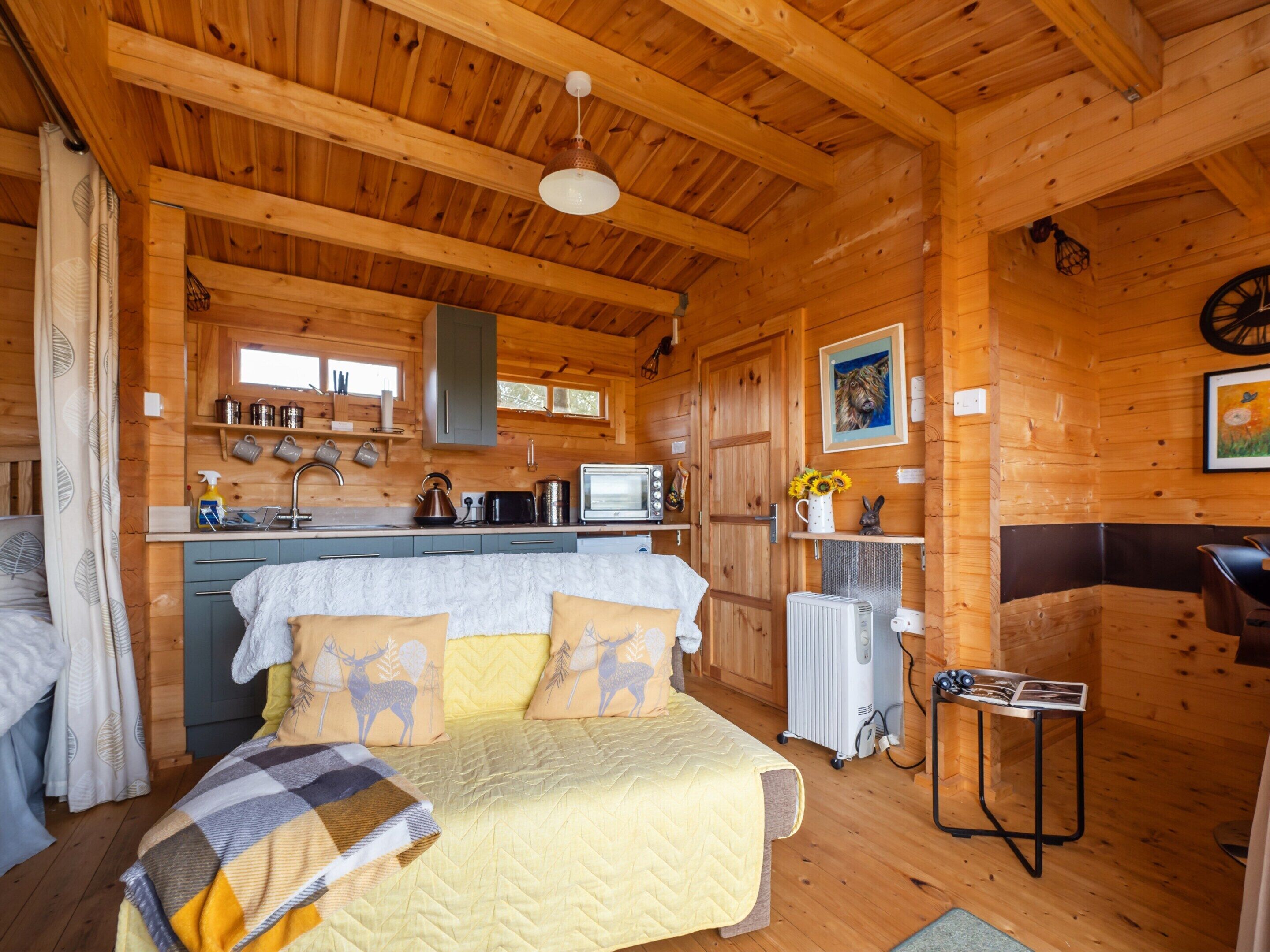 A cozy cabin interior with a bed, kitchenette, and a small table.