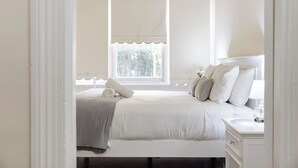 Un dormitorio con cama, almohadas, una mesita de noche y una ventana con vistas a zonas verdes.