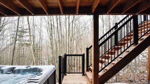 Eine Holzterrasse mit Whirlpool, einer Treppe und bewaldeter Landschaft.