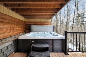 A wooden deck with a hot tub, a step stool, and a railing.