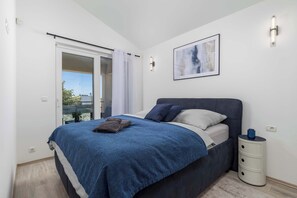 Un dormitorio con una cama, una mesita de noche, una lámpara de pared y una ventana con vistas.