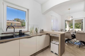 A modern kitchen with a built-in island, a sink, and a dining area with chairs and a table. - Villa Luxoria (Peroj)