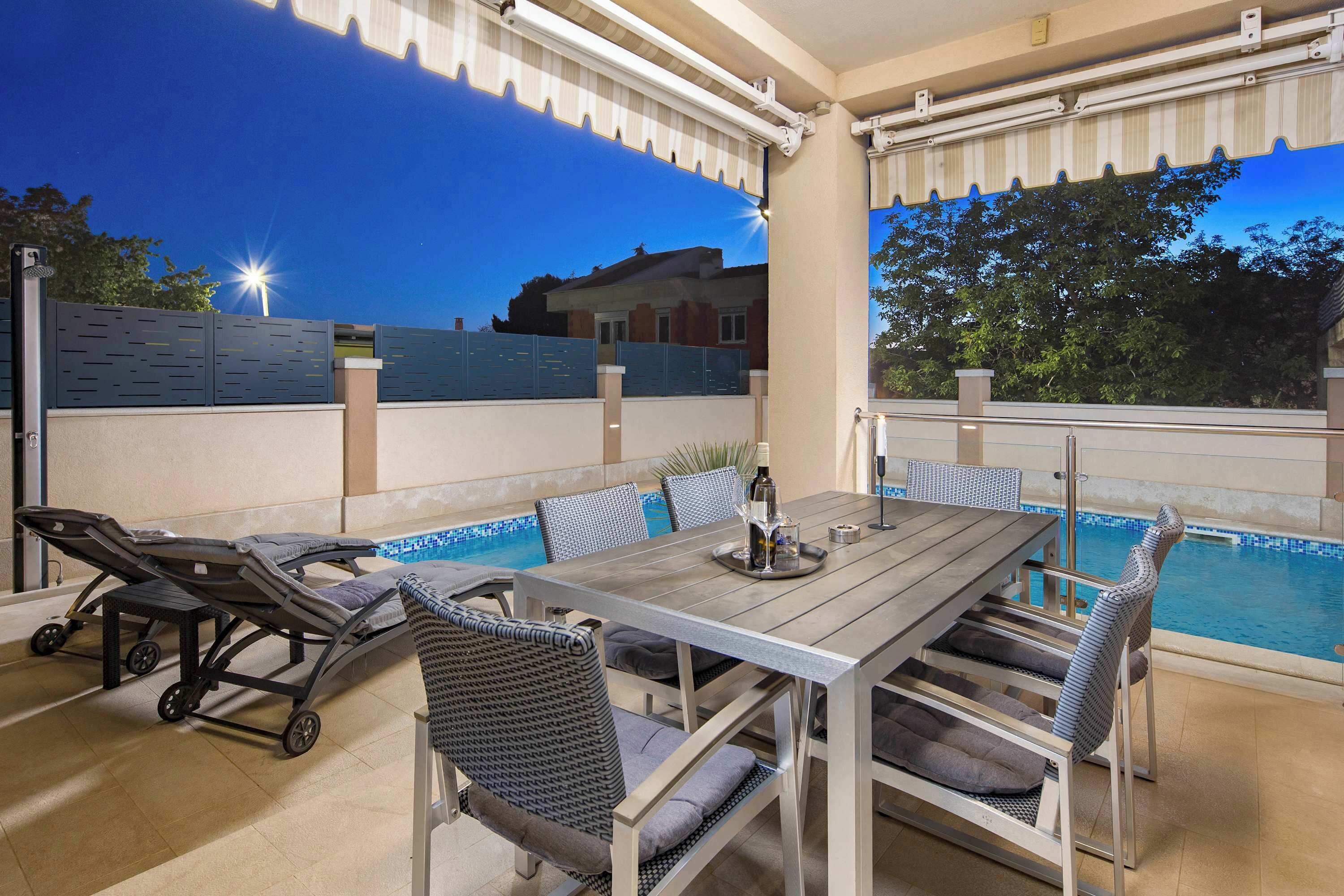 An outdoor patio with a pool, a dining table, chairs, and a reclining chair.