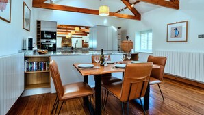 Uma sala de jantar espaçosa com uma mesa e cadeiras de madeira, uma cozinha ao fundo e um teto alto com vigas aparentes.