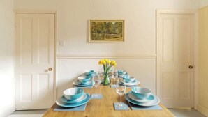 Ein Esstisch ist gedeckt mit blauen Tellern und Gläsern, eine Vase mit gelben Blumen und ein gerahmtes Bild an der Wand.