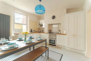 A modern kitchen with white cabinets, a blue hanging light, and a dining area with a table set for four.