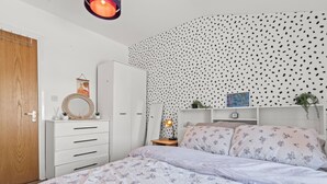 Un dormitorio con cama, armario, espejo, mesita de noche con lámpara y pared con diseño de hojas.