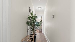 Un pasillo estrecho con un tendedero de madera, una planta en maceta y un radiador.