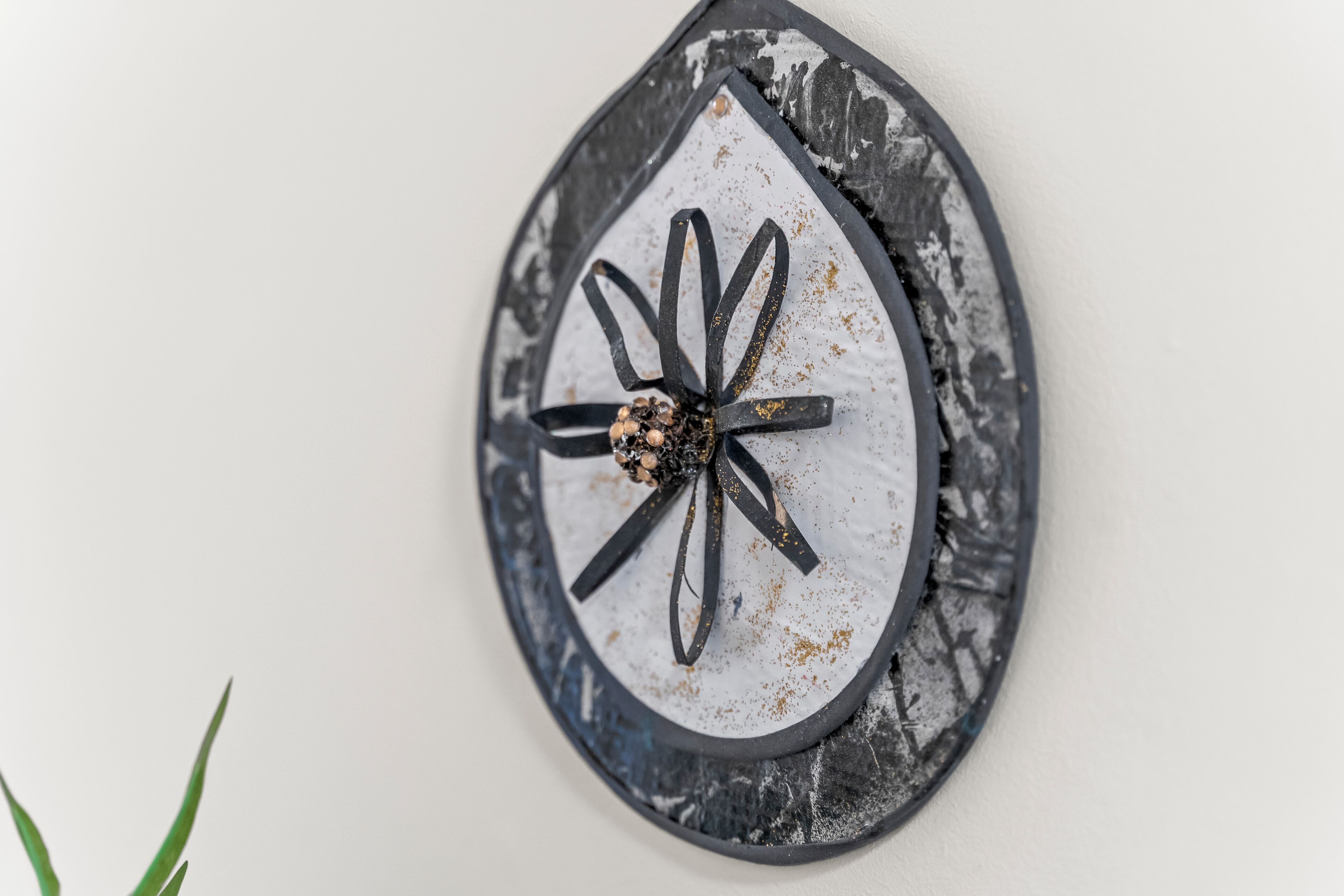 A wall-mounted decorative piece with a rustic, distressed look, featuring a central floral design and a black frame.