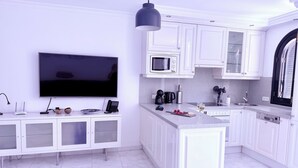 Cocina moderna con armarios blancos, un televisor de pantalla plana, una cafetera y una copa de vino sobre la encimera.