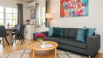 Een moderne woonkamer met een grijze bank, een ronde houten salontafel en een kleurrijk abstract schilderij aan de muur.