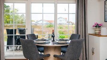 Een eethoek met een ronde tafel, twee stoelen en uitzicht op huizen door grote ramen.