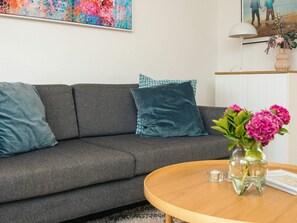 A modern living room with a grey sofa, teal cushions, a wooden coffee table, and a vase with pink flowers. - 4 Star Holiday Home in Laeso (Læsø)