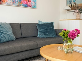 Una sala de estar moderna con un sofá gris, cojines turquesa, una mesa de centro de madera y un jarrón con flores rosas.