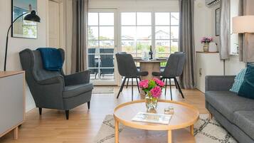 A modern living room with a round coffee table, two armchairs, a sofa, a dining table with chairs, and a view through large windows.