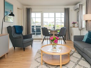 A modern living room with a round coffee table, two armchairs, a sofa, a dining table with chairs, and a view through large windows. - 4 Star Holiday Home in Laeso (Læsø)