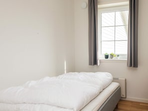 A single bed with a white mattress and grey bedding, a window with grey curtains, and a radiator below the window. - 4 Star Holiday Home in Laeso (Læsø)
